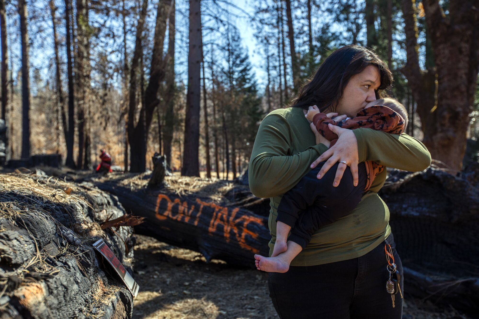 A woman kisses a baby she is holding amid wildfire damage.