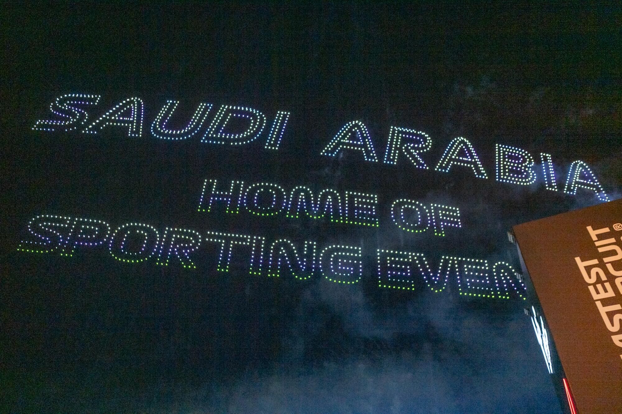 A light show in the sky spells out "Saudi Arabia: Home of sporting events." 
