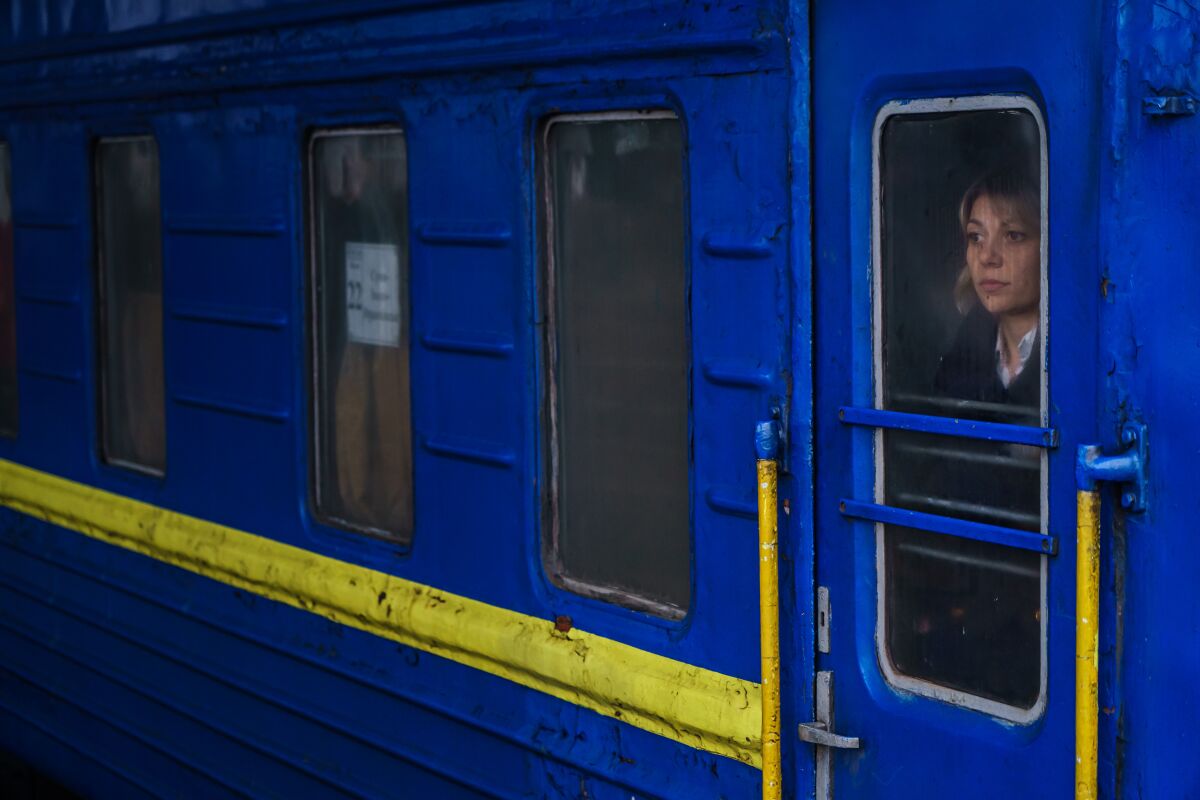 A woman's face is seen through the dirty glass of a bright blue train car. 