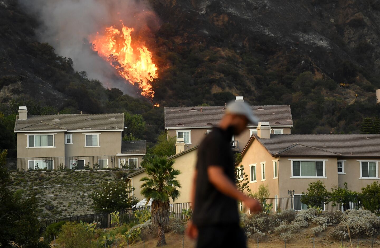 A man walks by a row of homes as the Ranch Fire burns in the hills of Azusa Thursday.
