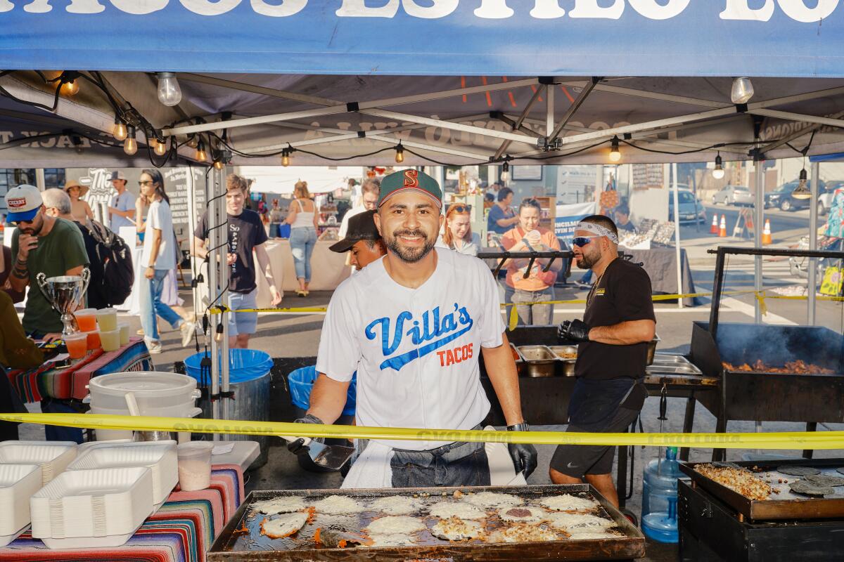 Owner Victor Villa of Villa's Tacos stands behind his taco stand, smiling at the camera, in Highland Park