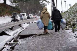 People walk the snow-covered street in Wajima in the Noto peninsula facing the Sea of Japan, northwest of Tokyo, Sunday, Jan. 7, 2024. Monday's temblor decimated houses, twisted and scarred roads and scattered boats like toys in the waters, and prompted tsunami warnings. (AP Photo/Hiro Komae)