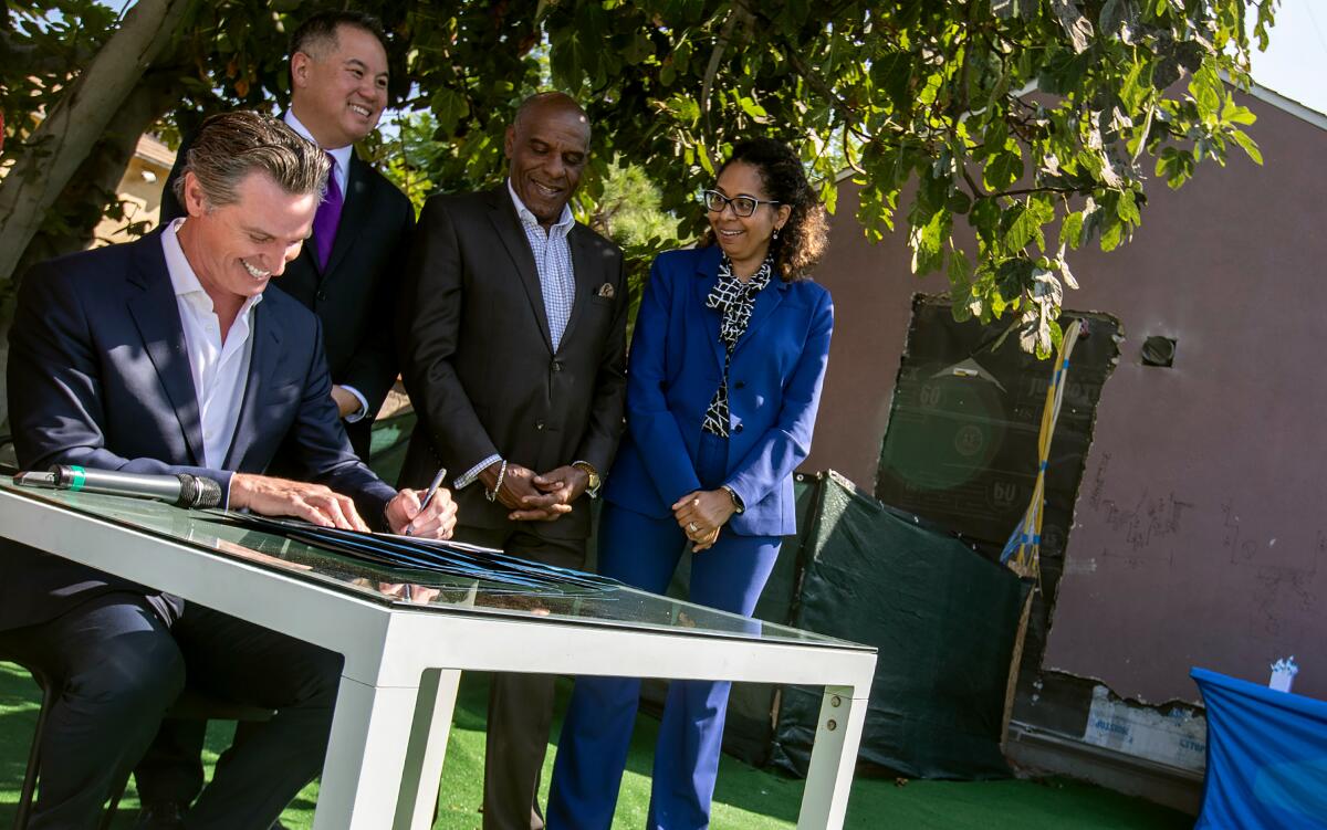 Gov. Gavin Newsom, left, signs a housing bill in the backyard of homeowner Felicia Smith this month in Los Angeles.