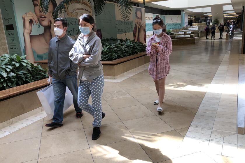 Shoppers wear maks as the walk through South Coast Plaza in Costa Mesa on Monday, March 16.