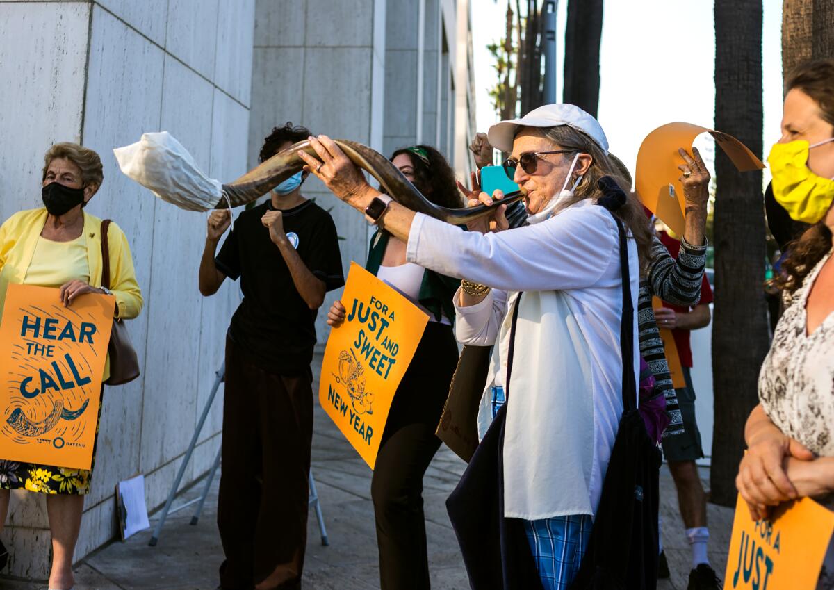 Climate protesters carry signs and blow a shofar