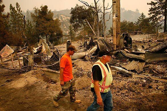 Caltrans employees who lived on the property of the Chilao Caltrans depot on Angeles Crest Highway walk past what remains of one of the three homes destroyed by the Station fire.