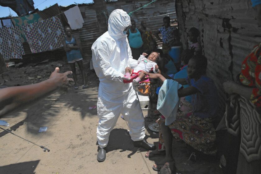A health worker carries an infant to an Ebola treatment unit in Monrovia, Liberia. Officials say the Ebola outbreak has sickened nearly 20,000 and killed about 7,700 of them.