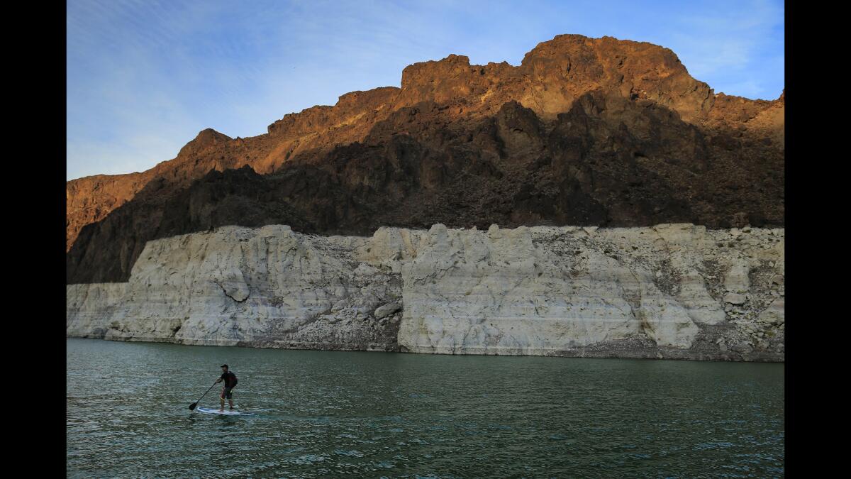 A stand-up paddle boarder takes a sunset cruise on July 2 near Hoover Dam at the Lake Mead National Recreation Area that is shared by Nevada and Arizona. A large bathtub-like ring circles the lake, marking the former water level.