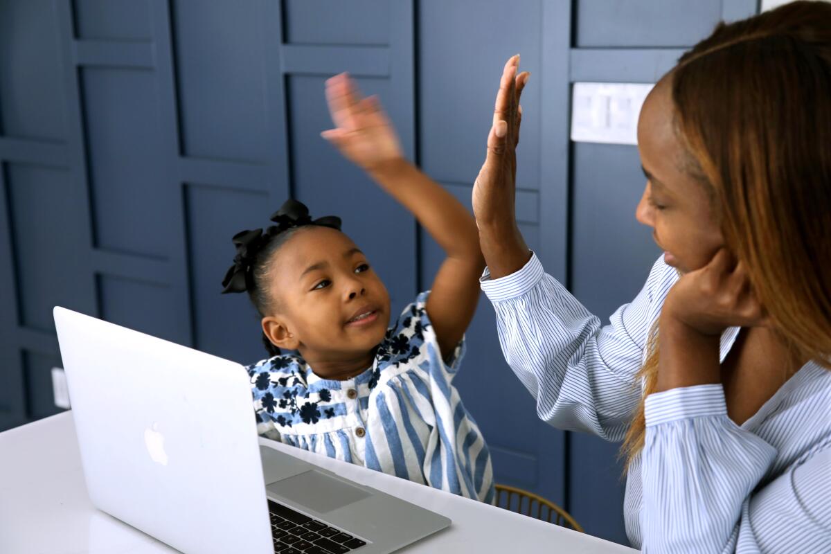 A little girl and a woman high-five each other in front of a laptop