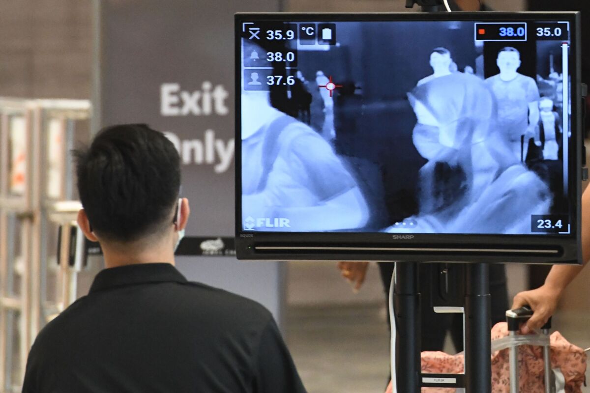 Travelers are seen on a monitor as they walk past a temperature screening check at Jewel Changi Airport in Singapore.