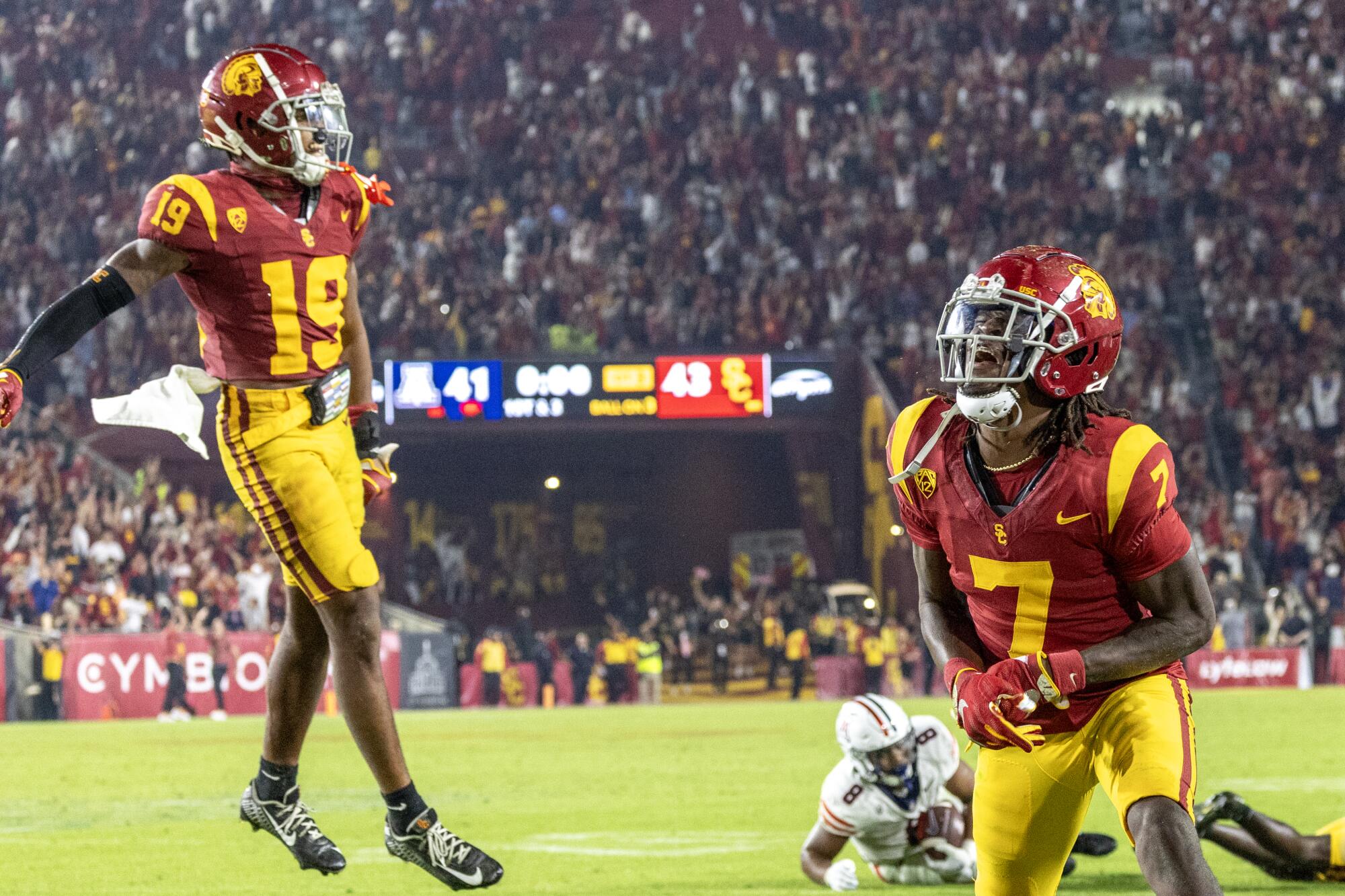 Trojans safeties Calen Bullock and Jaylin Smith jump and celebrate on the field near opponent on the ground.