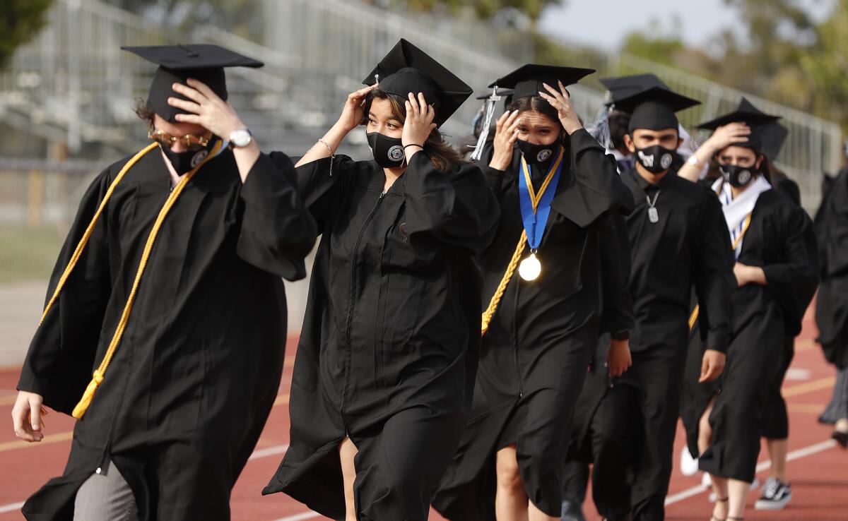 Early College High School graduates secure their caps during gusty winds as they enter Jim Scott Stadium Thursday, June 3.