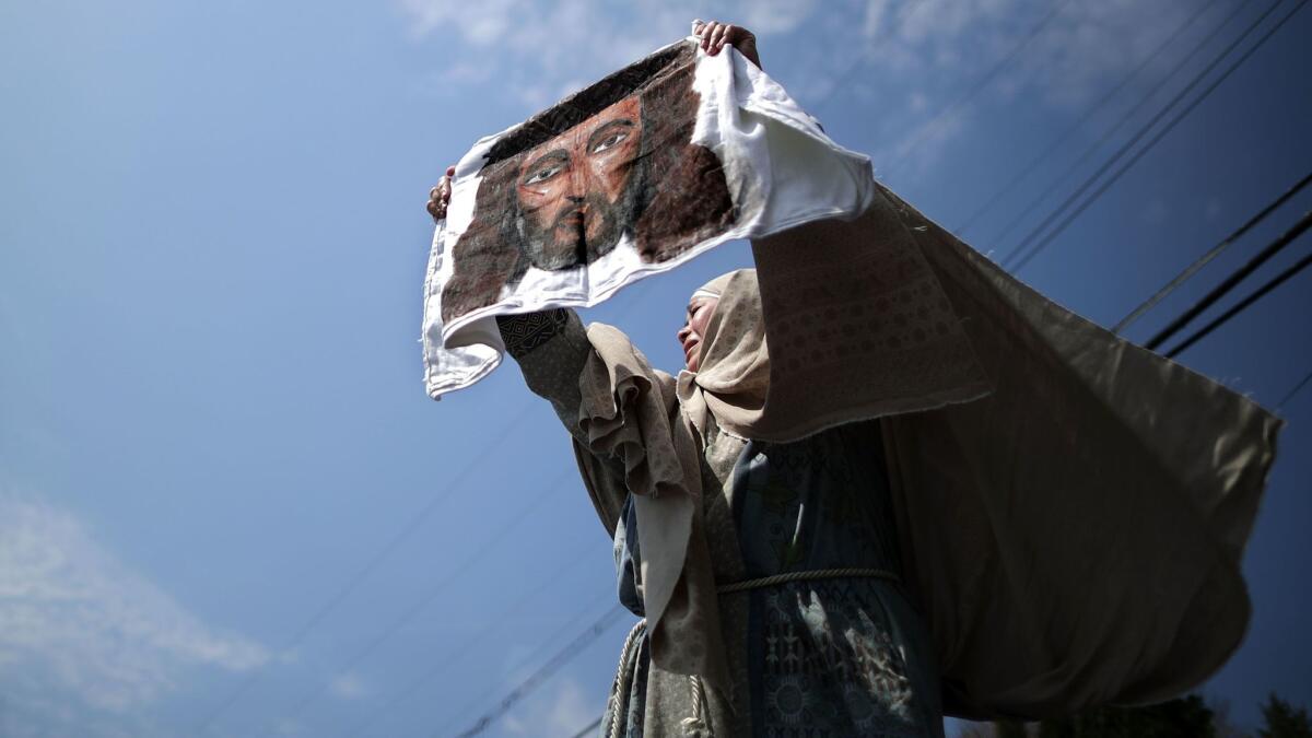 An actor portraying St. Veronica holds up an image of Jesus during a traditional Via Crucis, or Way of the Cross, procession on the Christian Good Friday holiday in Langley Park, Maryland.