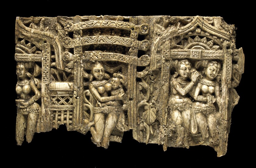 A close-up of an intricate ivory carving shows stylized human figures standing in doorways