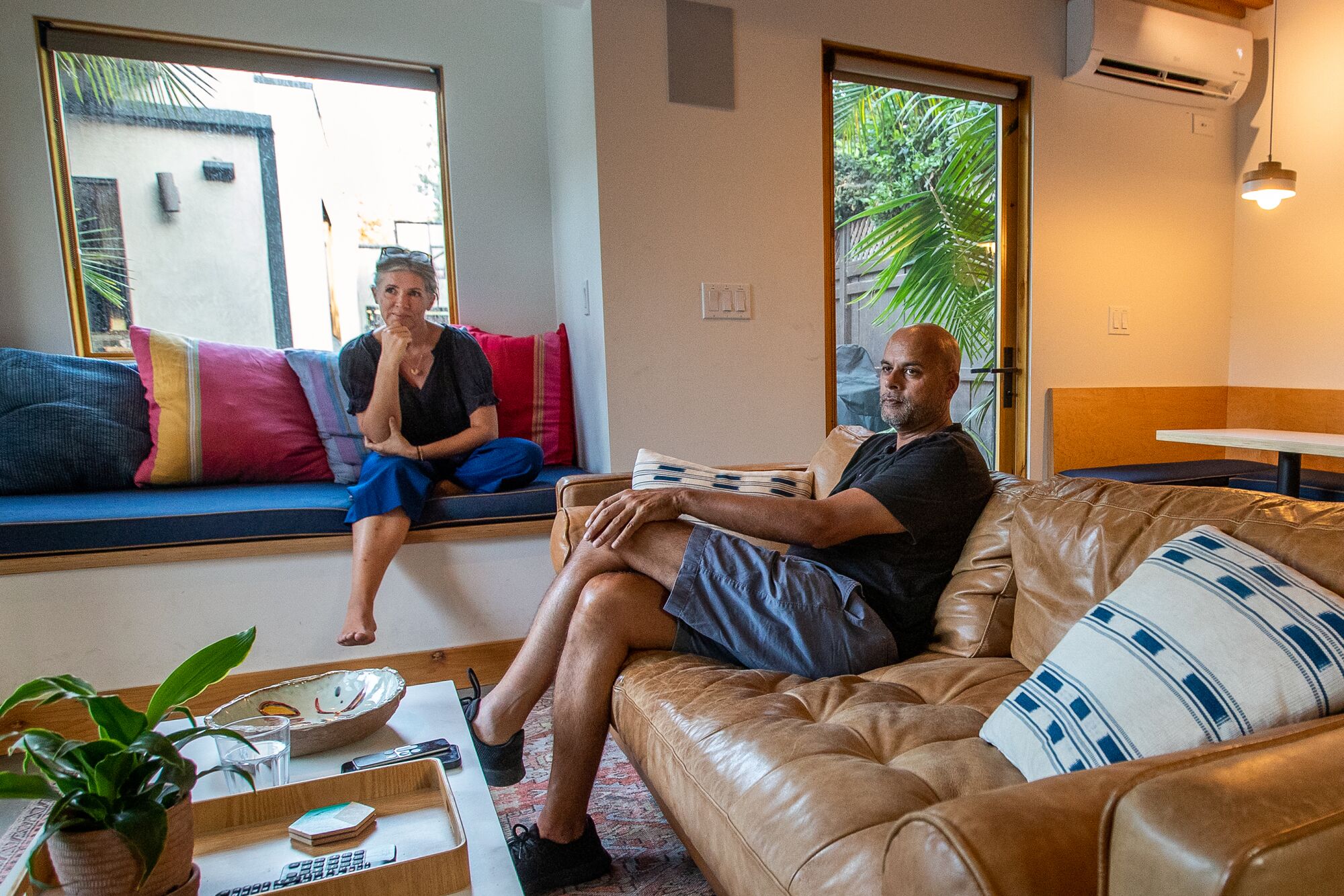A man sitting on a couch and a woman sitting on a window seat in a living room.