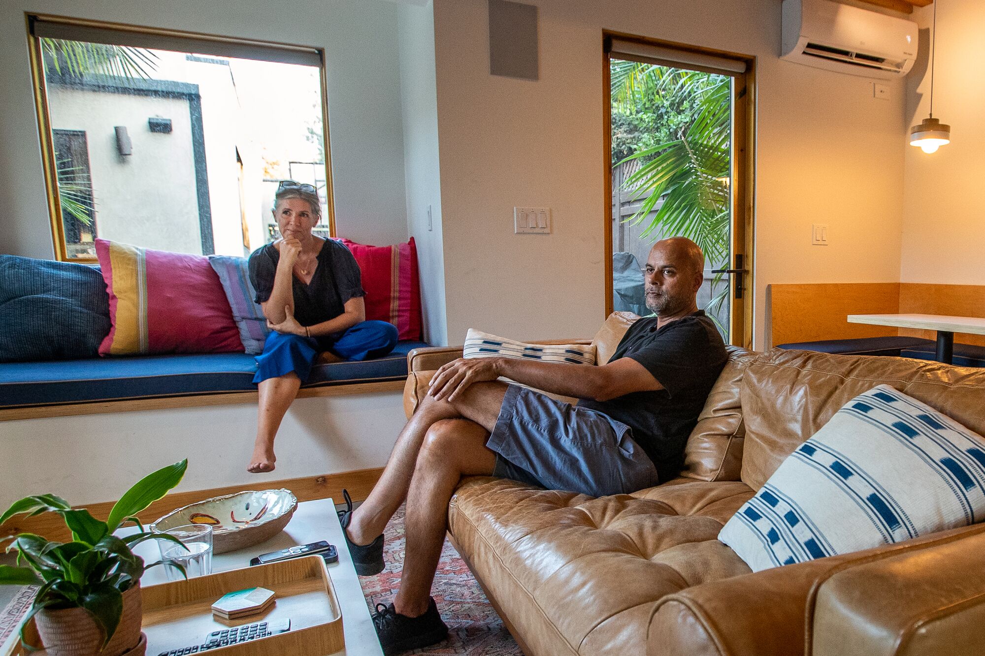Tiny ADU in Los Angeles is a pool house, office and gym 12 A man sitting on a couch and a woman sitting on a window seat in a living room.