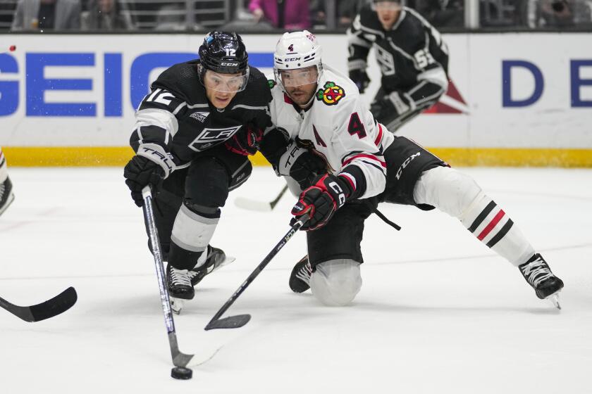 Los Angeles Kings left wing Trevor Moore (12) and Chicago Blackhawks defenseman Seth Jones (4) reach for the puck during the second period of an NHL hockey game Thursday, April 18, 2024, in Los Angeles. (AP Photo/Ashley Landis)