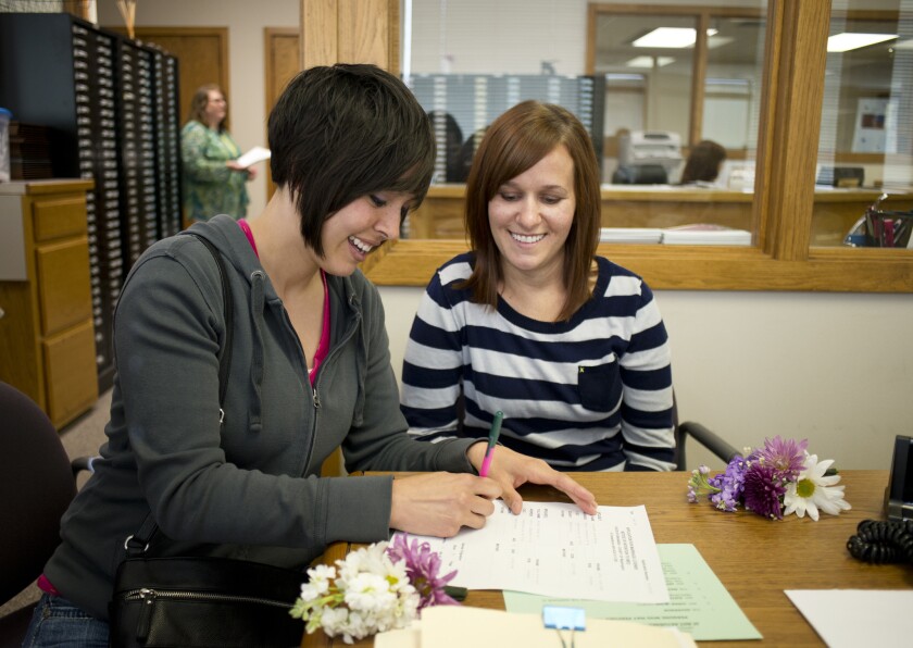 Beth Moore, left, signs her marriage license as her partner, Abby Hill, looks on at the Washington County Courthouse in Fayetteville, Ark.