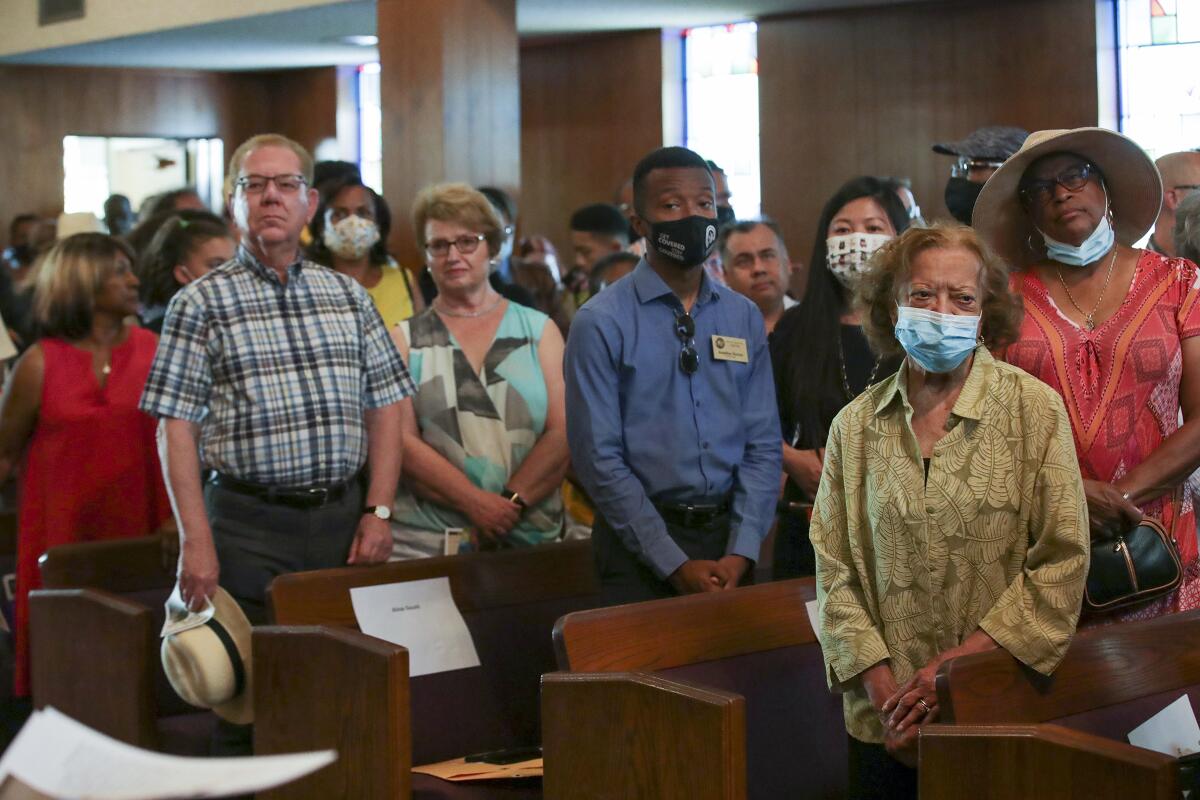 A diverse crowd stands amid pews.