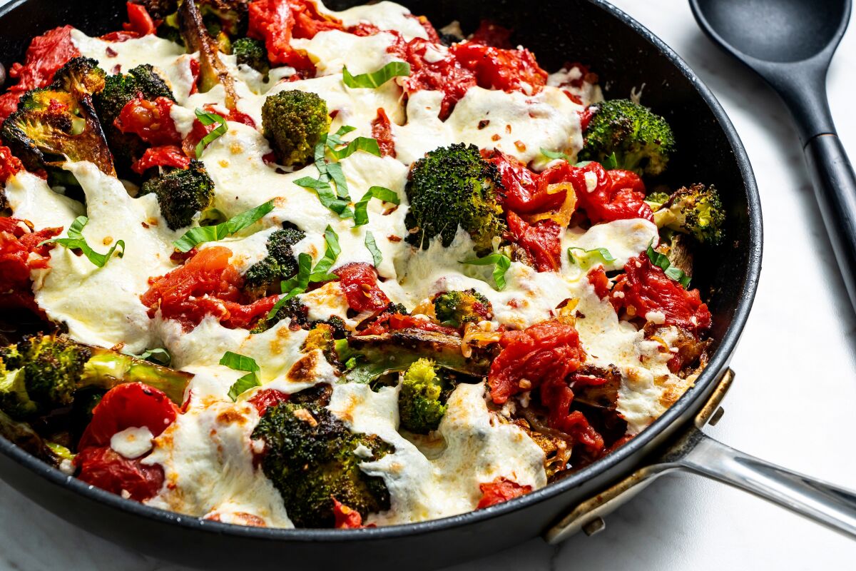 A skillet holds seared broccoli with crushed tomatoes, cheese and spices.