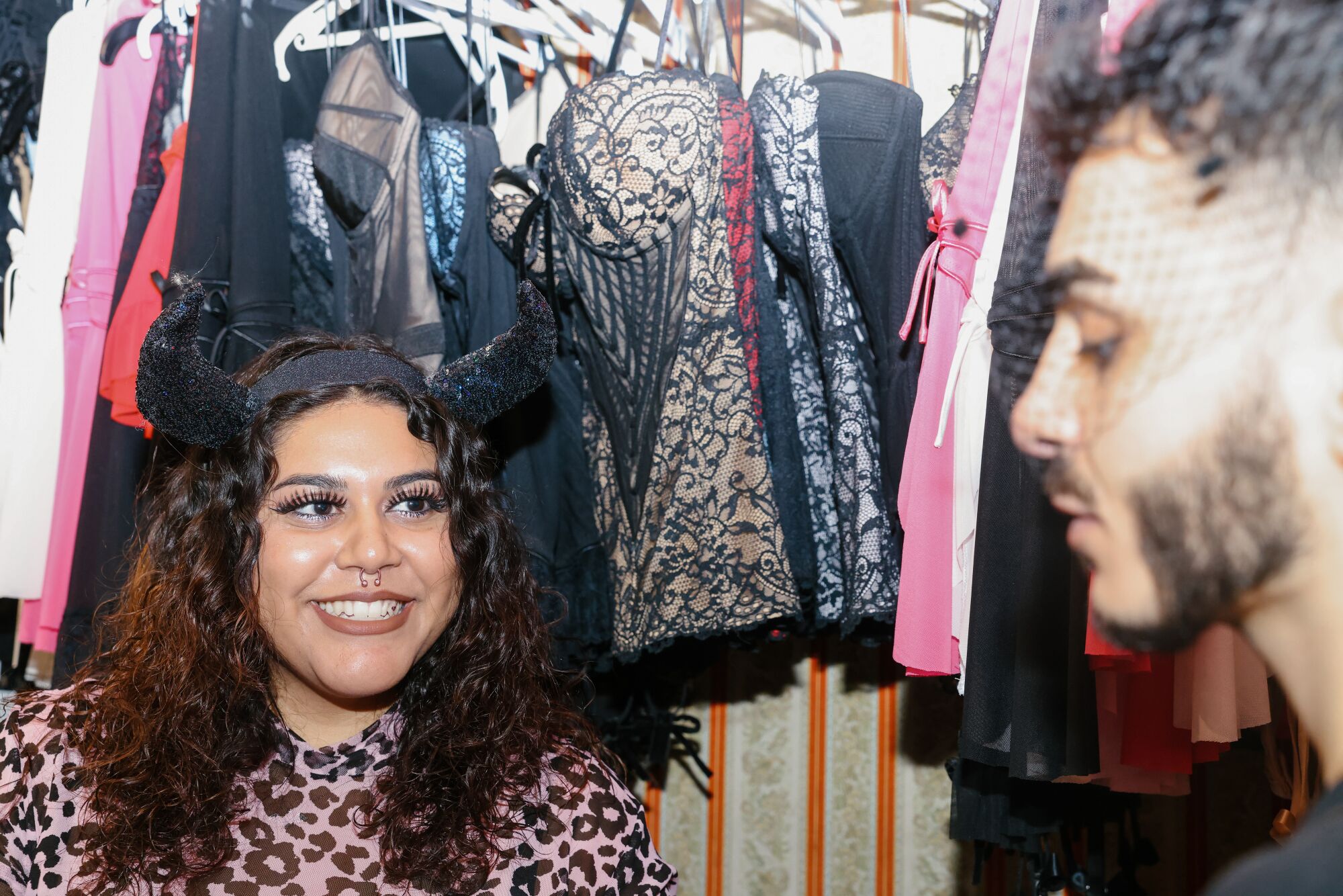A woman wearing a black fabric horned headband smiles at a man standing amid lingerie for sale in a store.