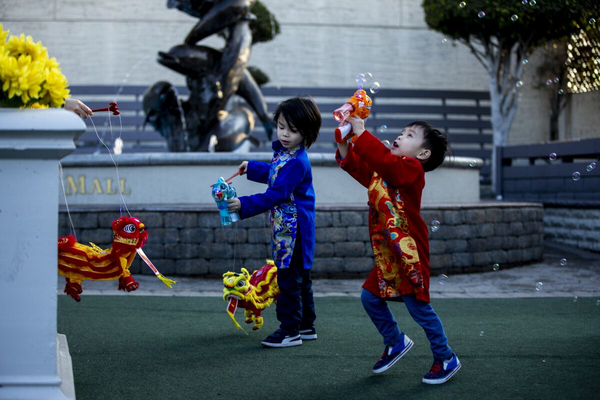Children in traditional Vietnamese dress play with bubbles and toy dragons.