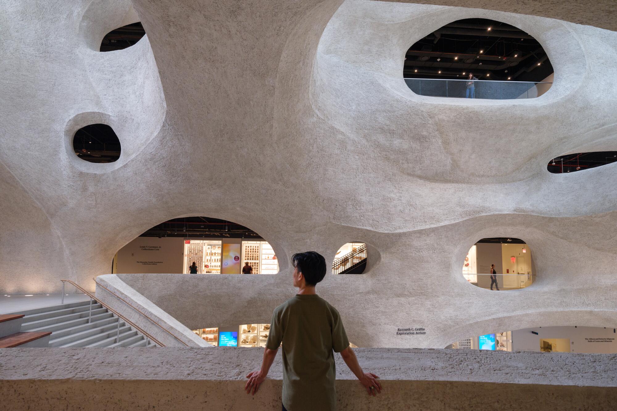 A young man stands at a balcony overlooking a large, cave-like atrium filled with the echoes of children's voices