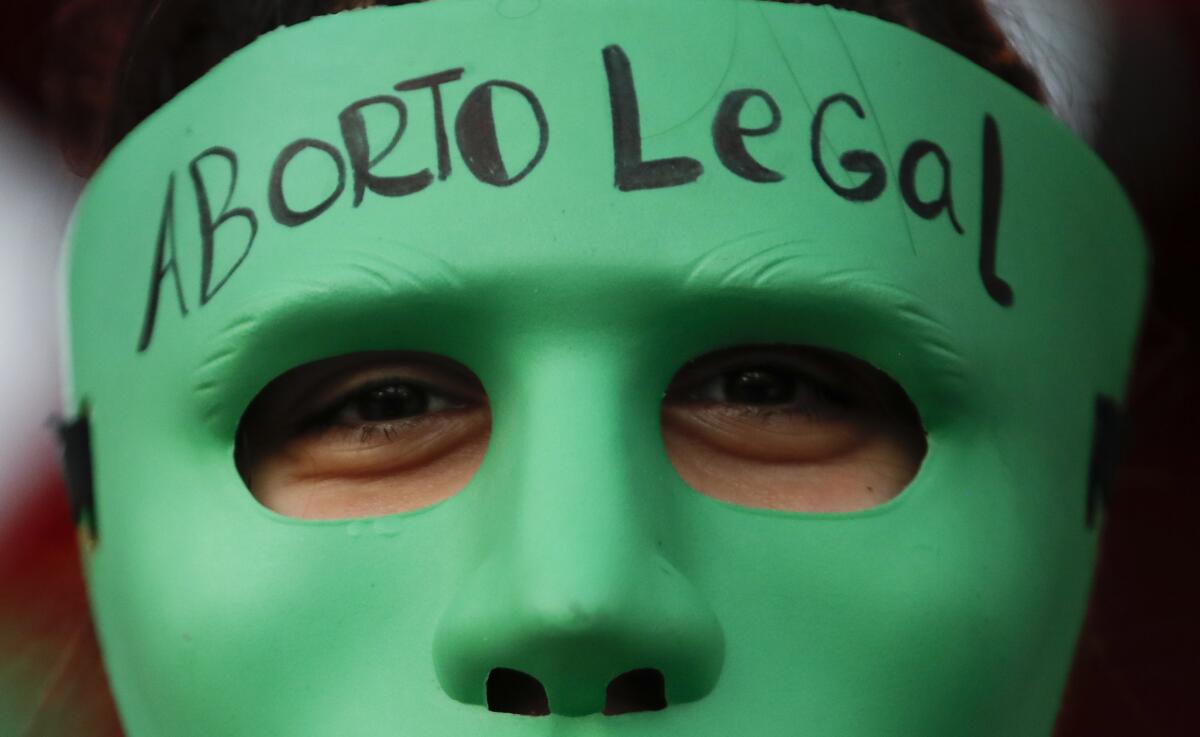 An abortion rights activist wears a mask with text that reads in Spanish "Legal Abortion" 