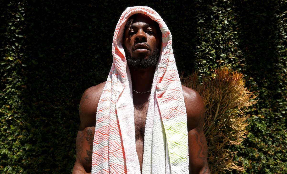 A shirtless man stands in the sun with a towel draped over his head