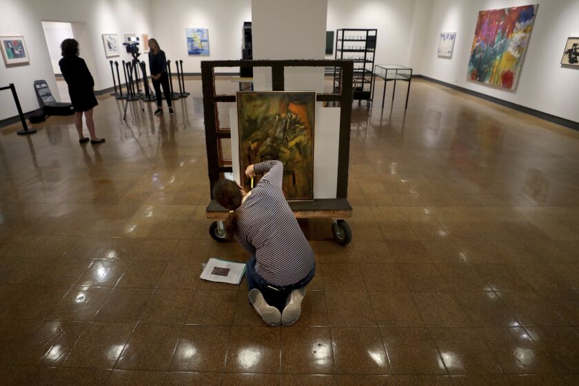 Registrar Kristen Schmidt takes stock of the painting "Seated Man" by Elaine de Kooning, wife of Willem de Kooning, while working on the exhibit Abstract Perspectives in Mid-Century Art, which will display in conjunction with the return of Willem de Kooning's "Woman-Ochre" at the University of Arizona Museum of Art, Tucson, Ariz., Wednesday, Sept. 28, 2022. (Kelly Presnell/Arizona Daily Star via AP)