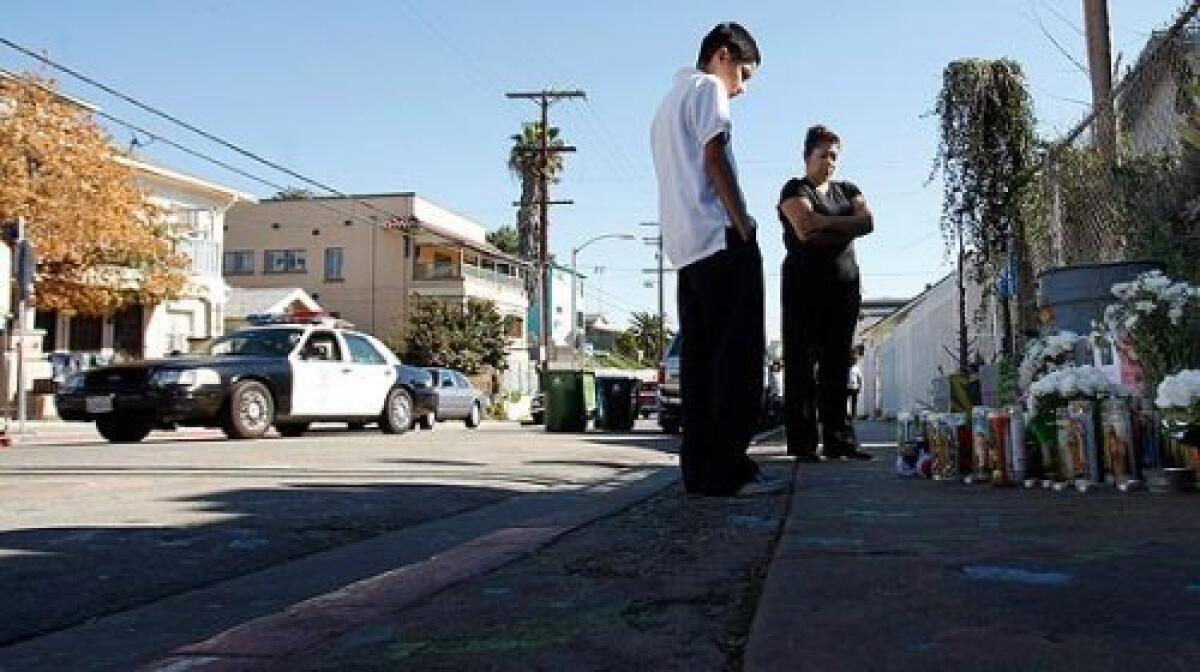 An LAPD cruiser drives through the neighborhood south of Echo Park as Hugo Gonzalez, 12, a relative of the victim, and Kathy Morales, whose 16-year-old brother was killed last year nearby, stand in front of the memorial for Robert Lopez Jr.