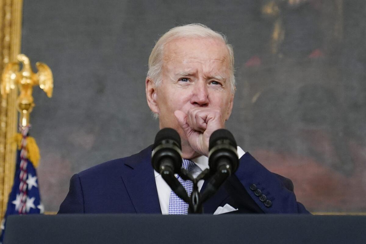 President Biden raises a hand to his mouth as he delivers an address.