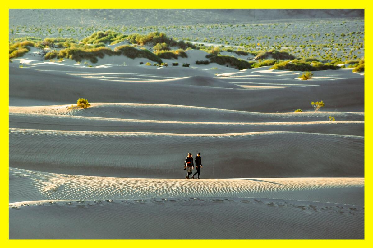 Two people walk across a sand dune