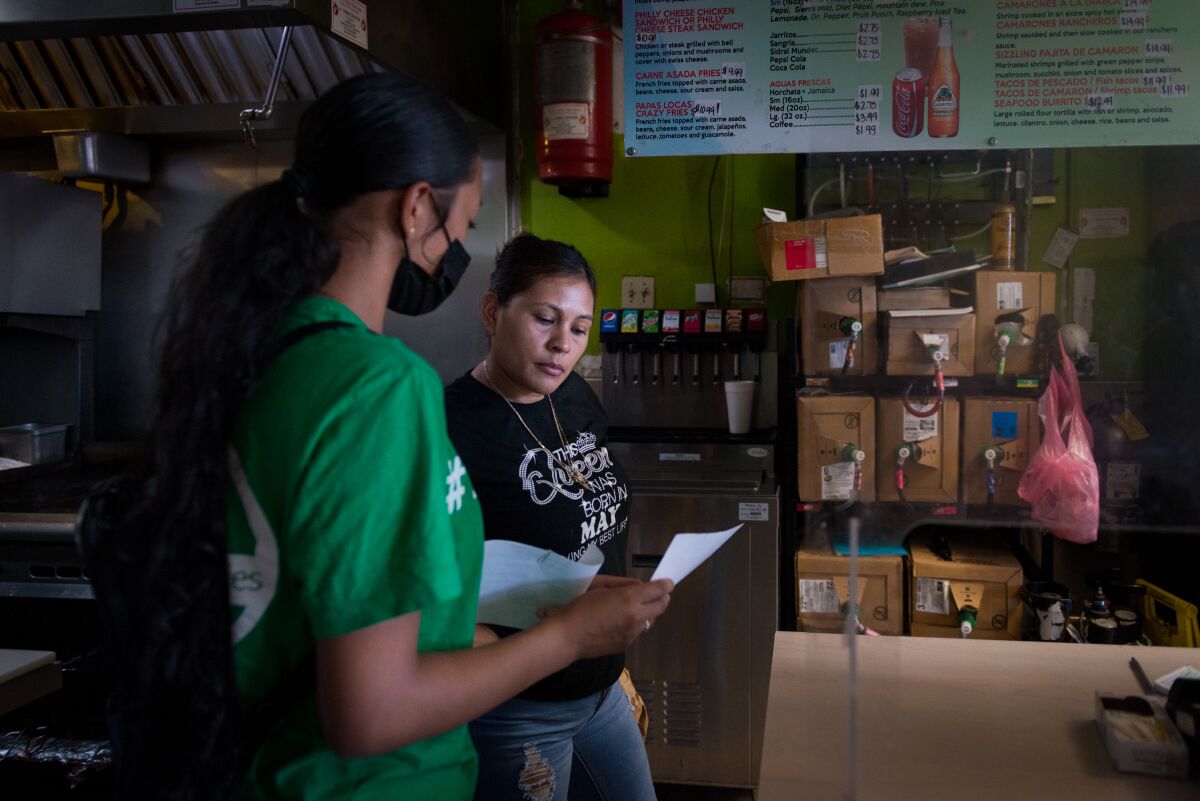 A person holds a sheet of paper and speaks to a worker at a restaurant