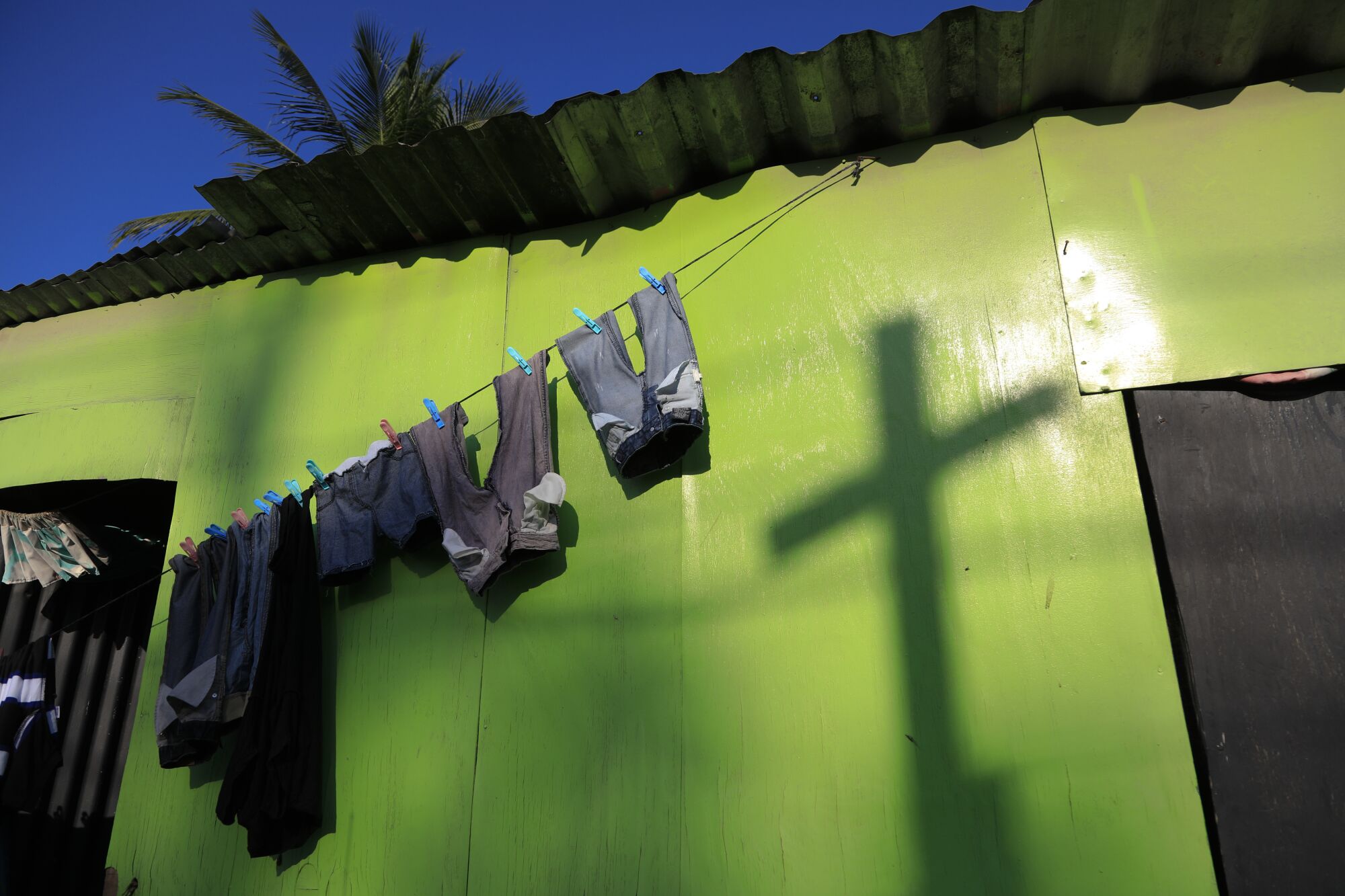 The shadow of a religious cross is cast next to a clothes line full of pants hanging to dry. 