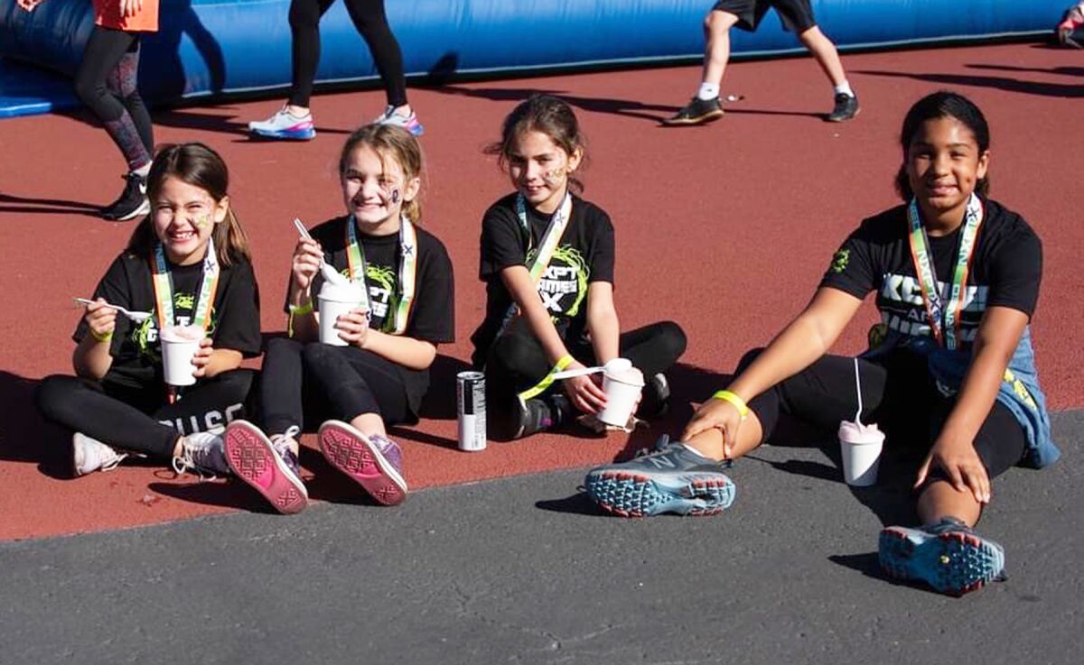 A group of girls proudly show off their medals while enjoying a treat after an interactive fitness event.
