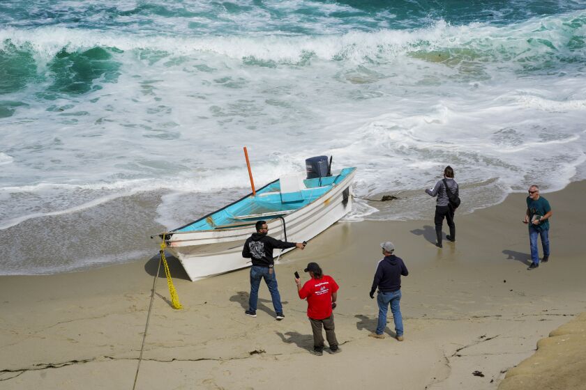 San Diego, CA - May 20: On Thursday, May 20, 2021 in San Diego, CA., investigators near ChildrenÕs Pool look over a small boat on the beach. Border Patrol says 15 people have been taken into custody after the boat came into shore near ChildrenÕs Pool. At least one person died and several people were rescued from the water after a suspected smuggling boat capsized off the La Jolla shore early Thursday, authorities said. (Nelvin C. Cepeda / The San Diego Union-Tribune)
