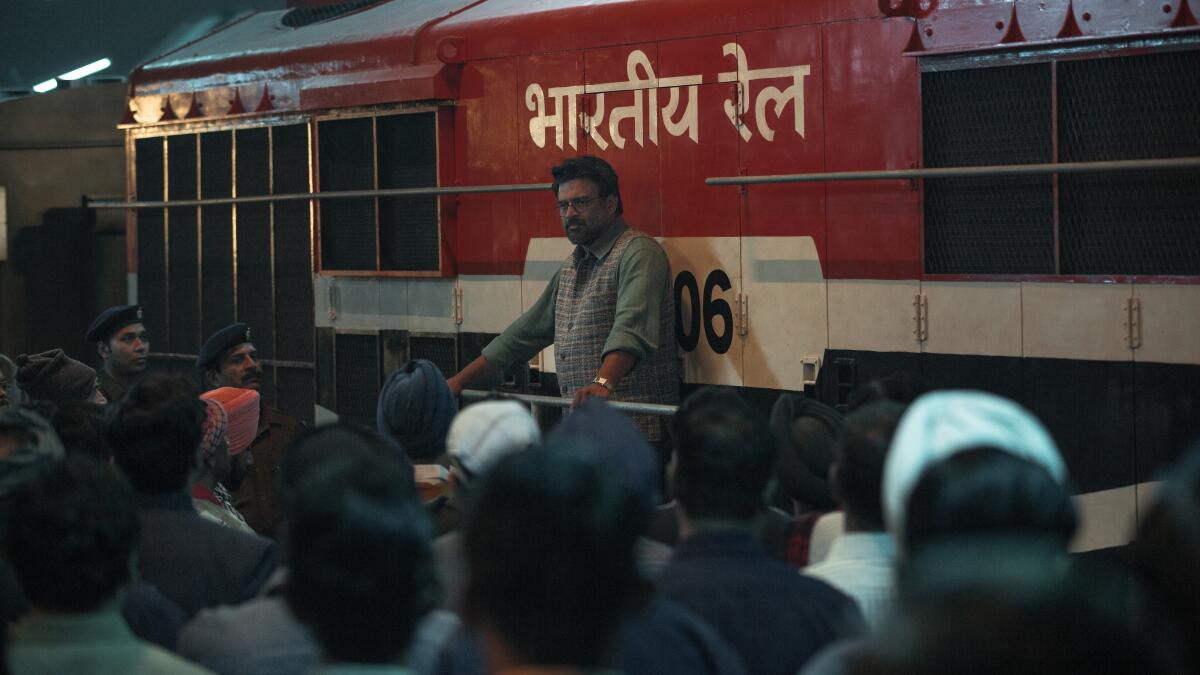 A man speaks to a crowd in a railway yard.