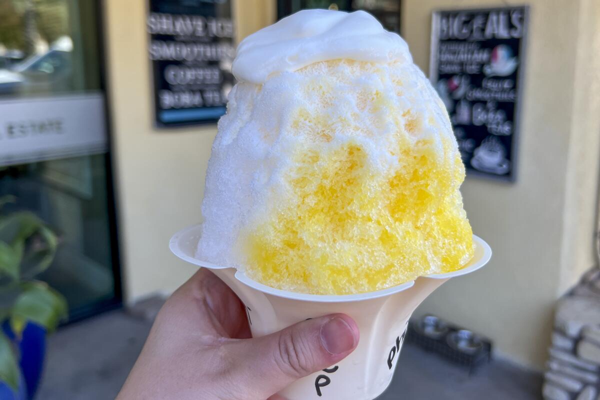 A hand holds up a heaping cup of yellow and white shave ice.