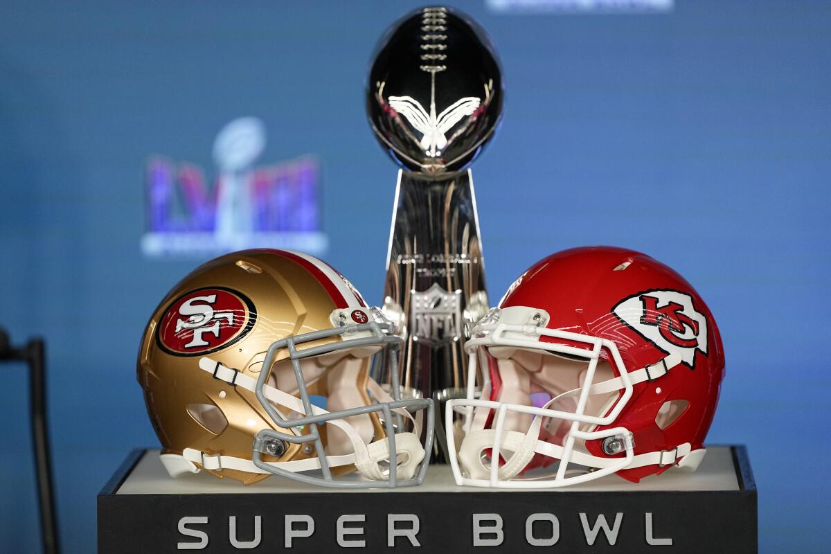 The Super Bowl trophy is flanked by San Francisco 49ers and Kansas City Chiefs helmets.