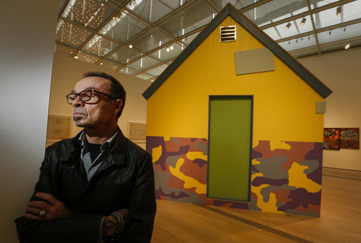 Artist Daniel Joseph Martinez stands before his scale model Unabomber cabin painted in bright shades of Martha Stewart paint