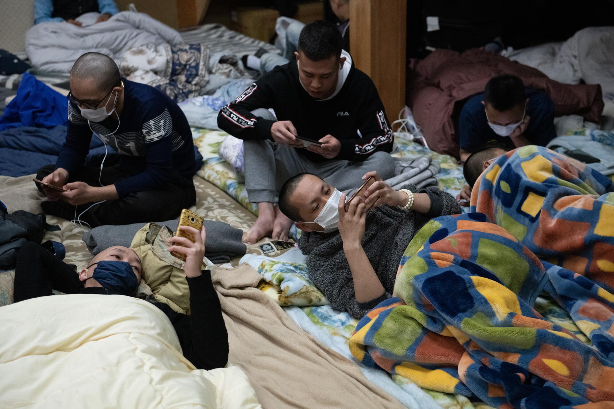 Several people reading their phones as they sit or lie on bedding on a floor