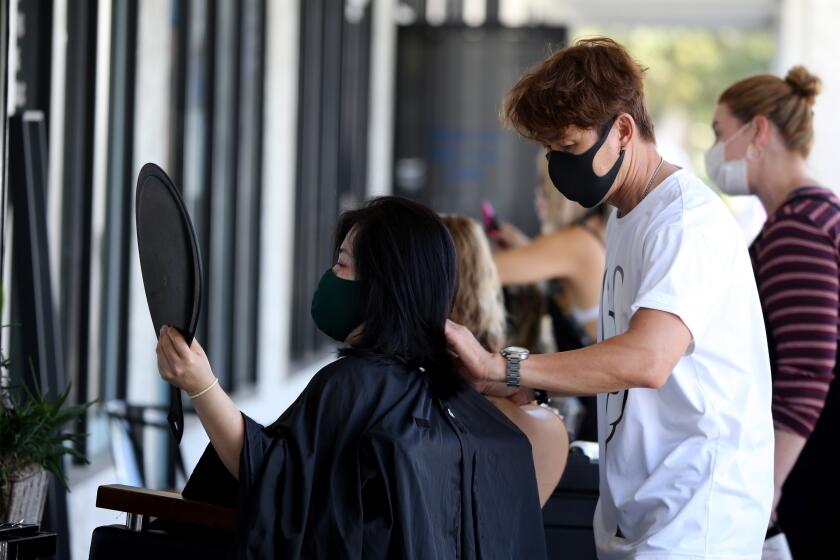 Travis Vu, 47 of Anaheim, finishes cutting the hair of client Thuy Ngo outside Travis Vu The Salon, in Fountain Valley on Saturday, Aug. 1, 2020. Vu is now able to operate in the open air following guidelines set by the city because of the coronavirus Covid-19.