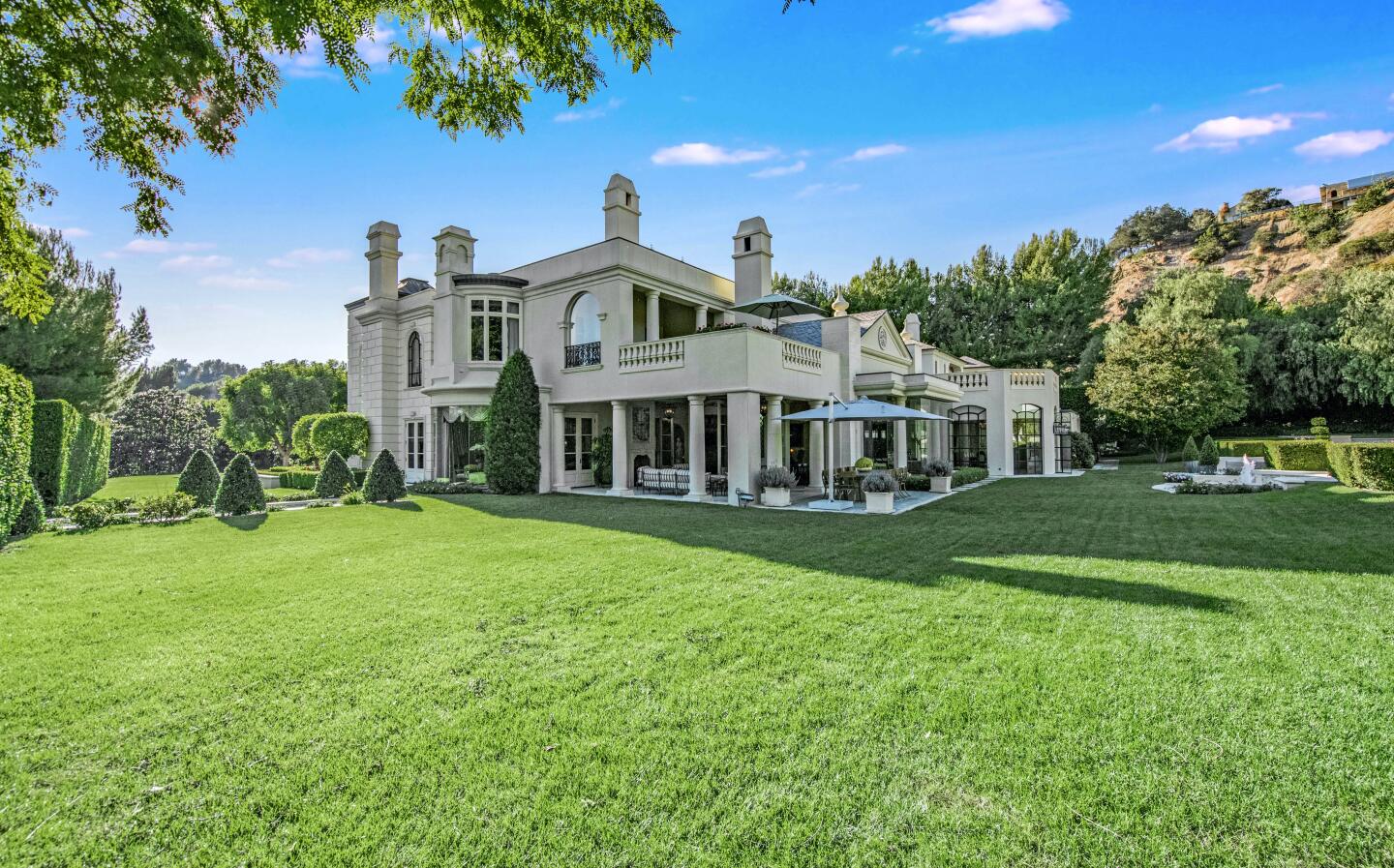 The grassy backyard with the home and a hill in the background.