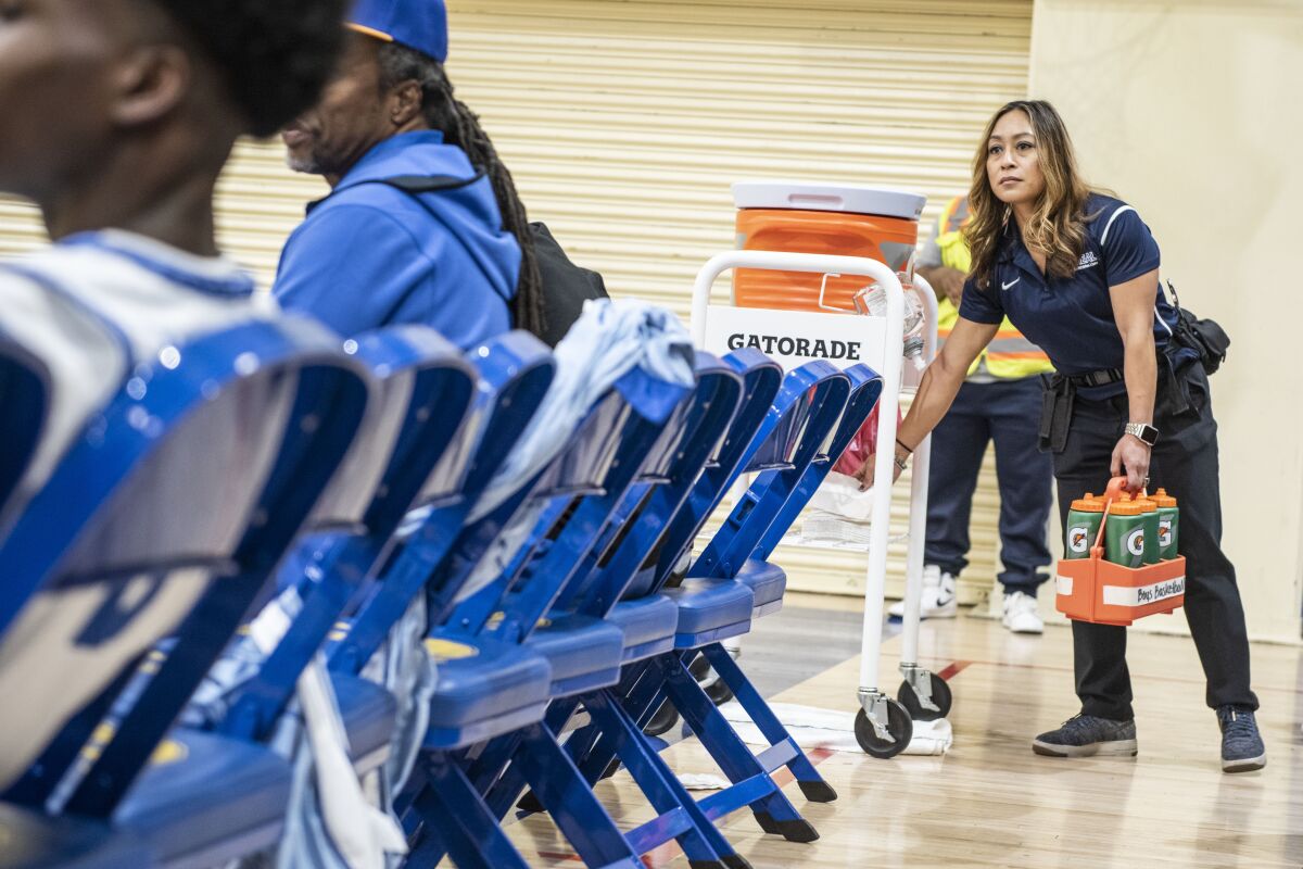 Crenshaw athletic trainer Ellen Kelly grabs towels and water bottles for the basketball players during a timeout at a game Jan. 24, 2020.