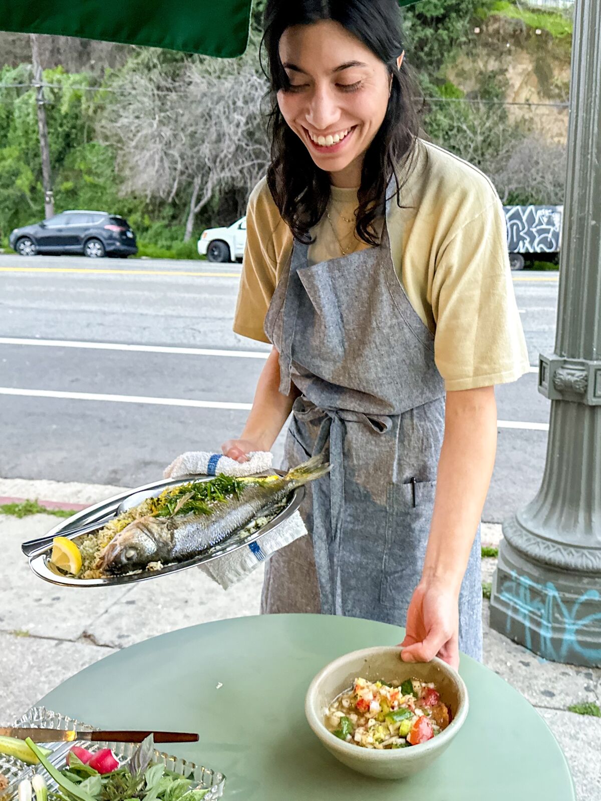 Misha Sesar places two plates of food on a table at an Azizam pop-up dinner celebrating Nowruz.