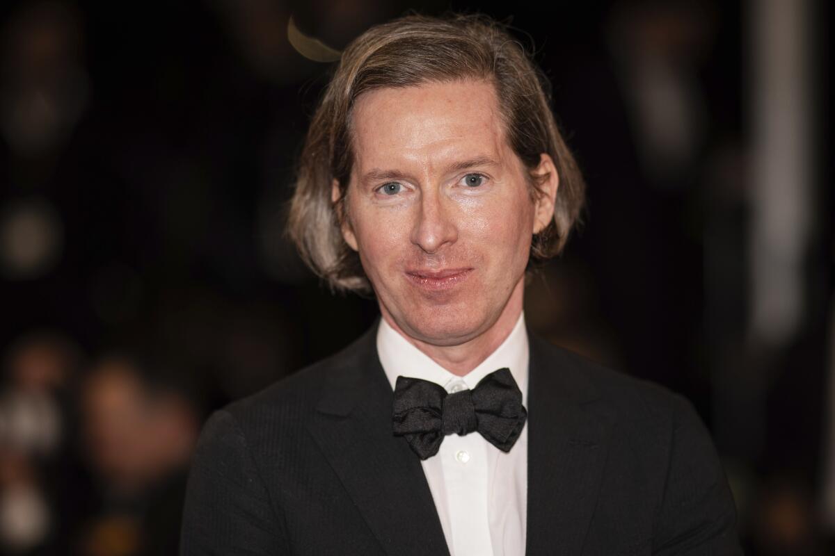 Wes Anderson wears a black tuxedo and bow tie on a red carpet.