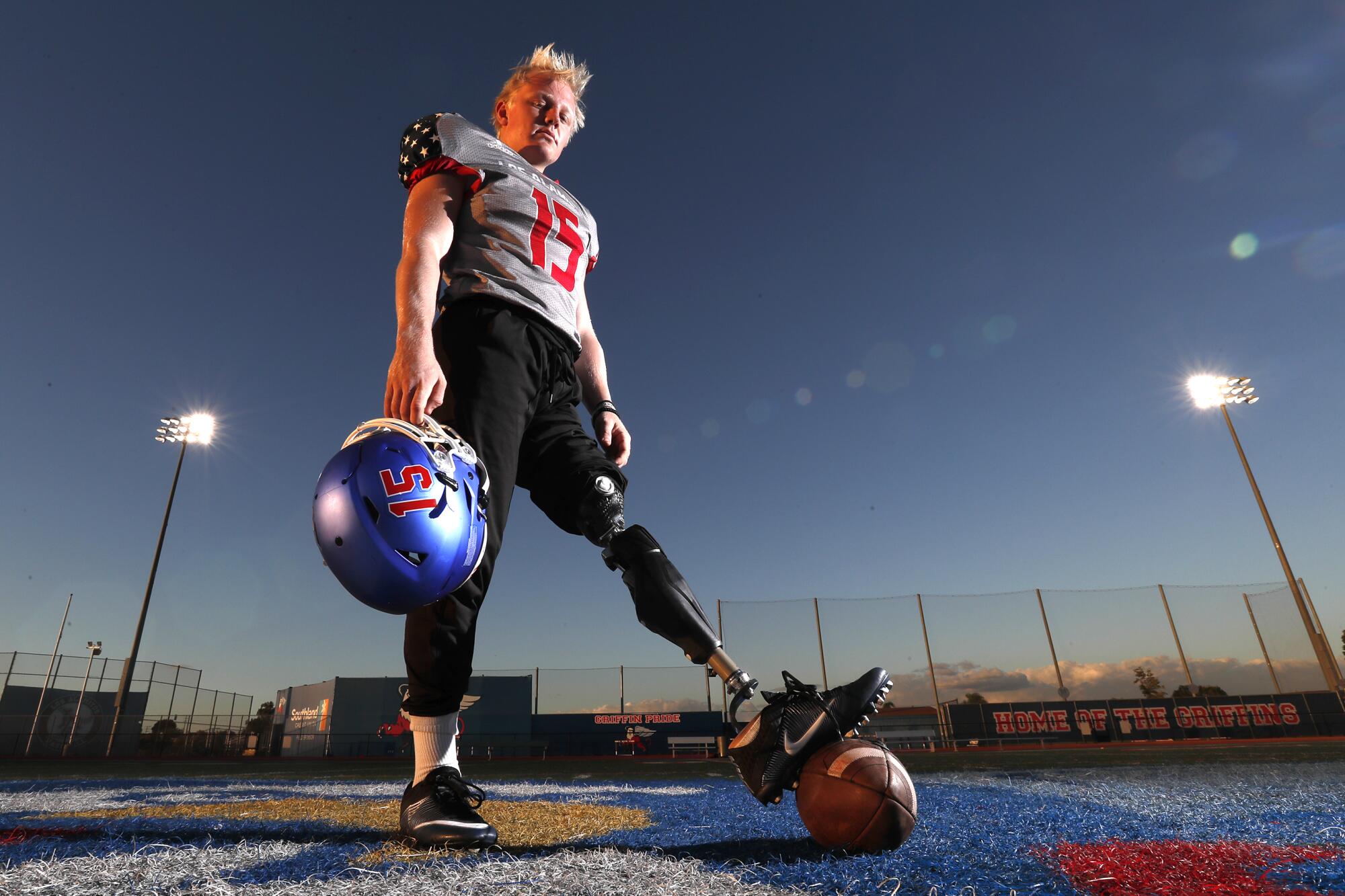Los Alamitos long snapper Carson Fox places his prosthetic leg on a football while standing on the field.