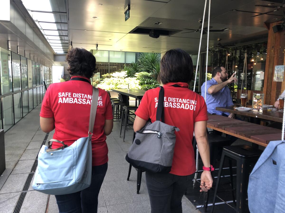 Safe-distancing ambassadors Rugayah Noordin and Fiona Tay, right, walk past a bar in Singapore.