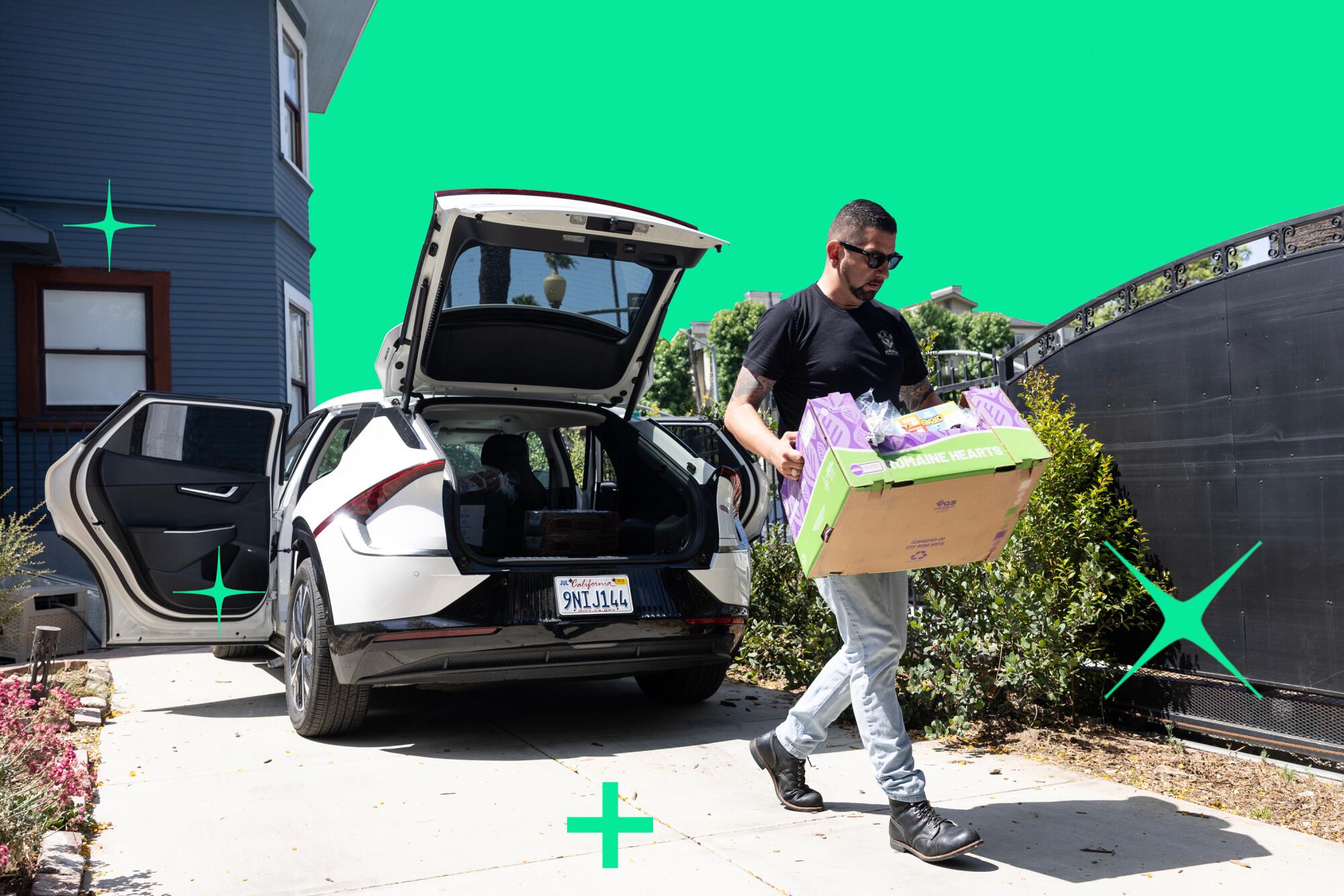 A man carries a box of groceries from a car in a driveway